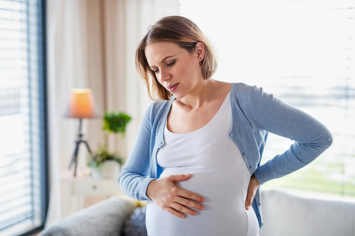 Sideways profile of a pregnant woman holding her belly in warm light
